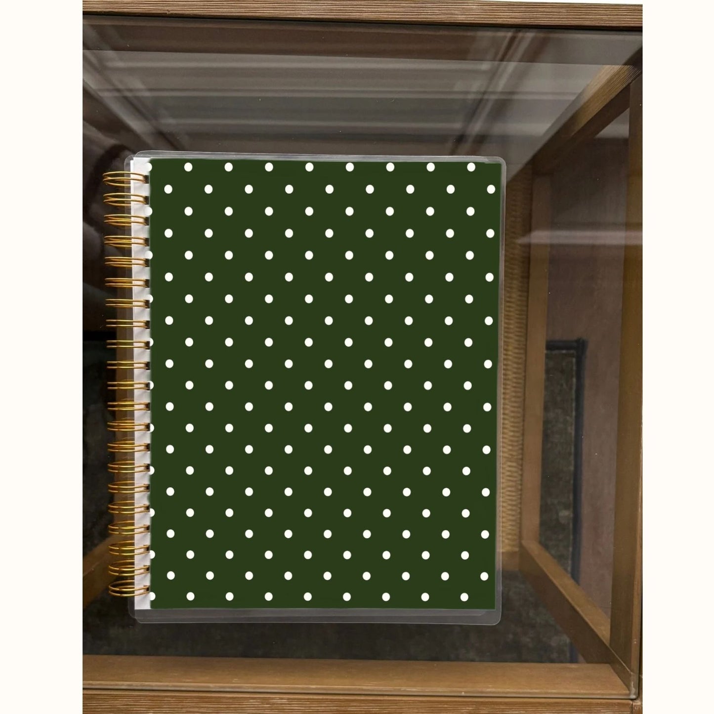 Notebook with green cover and white polka dots on a wooden shelf.