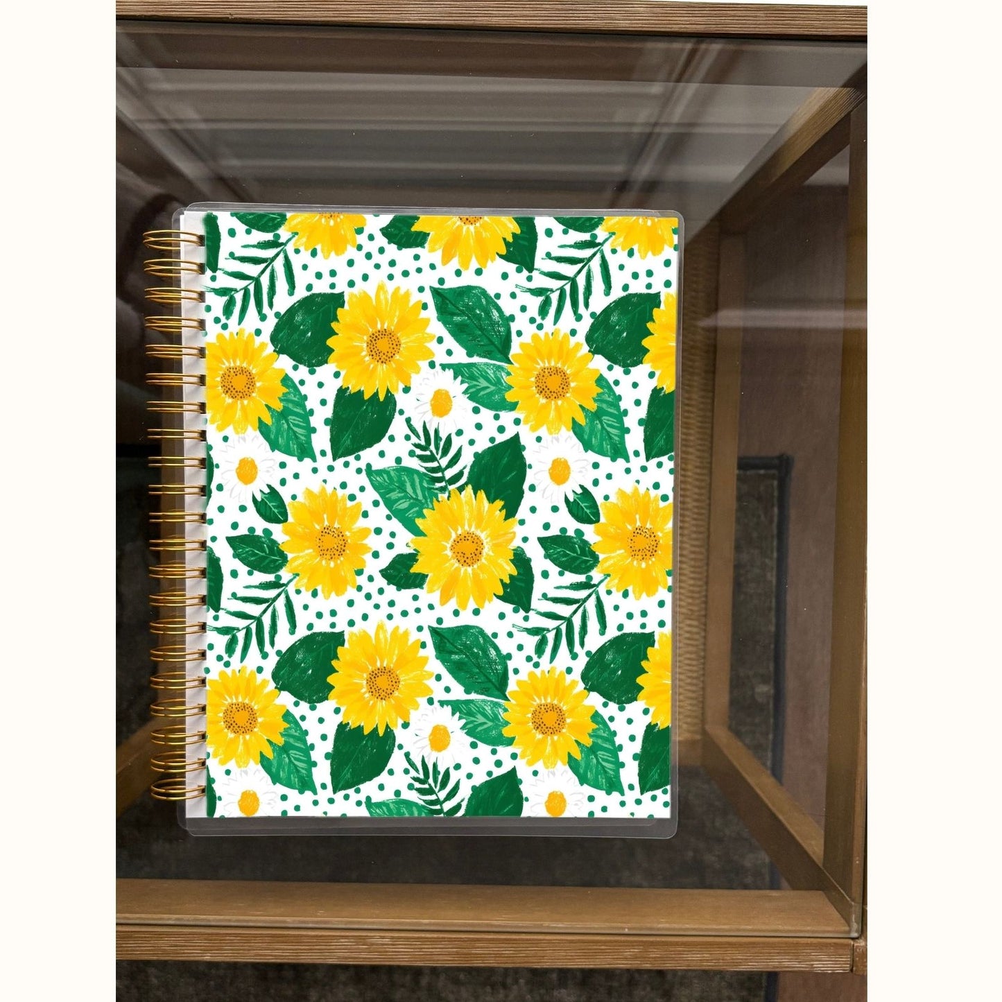 Notebook with yellow floral design on a white background, placed on a wooden surface.