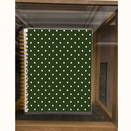 Notebook with green cover and white polka dots on a wooden shelf.