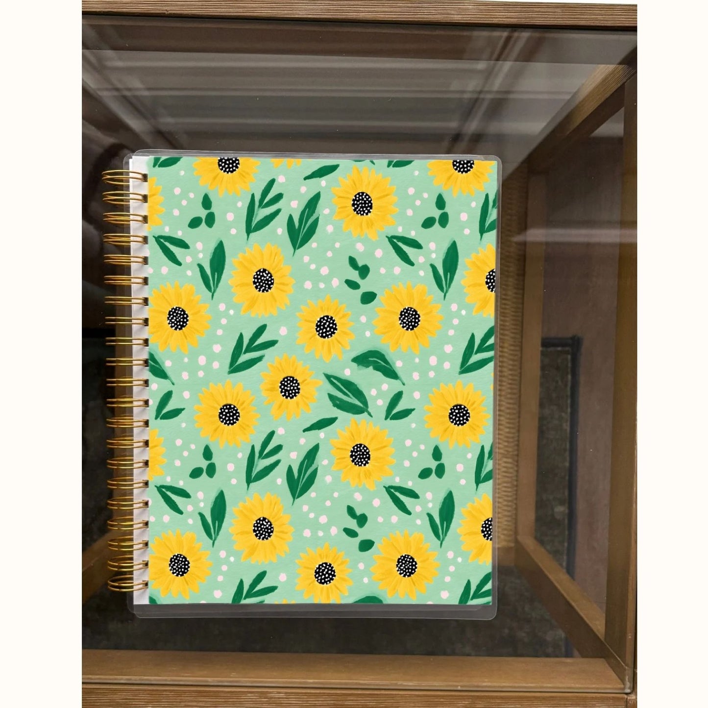 Notebook with sunflower pattern on a green background, placed on a wooden surface.